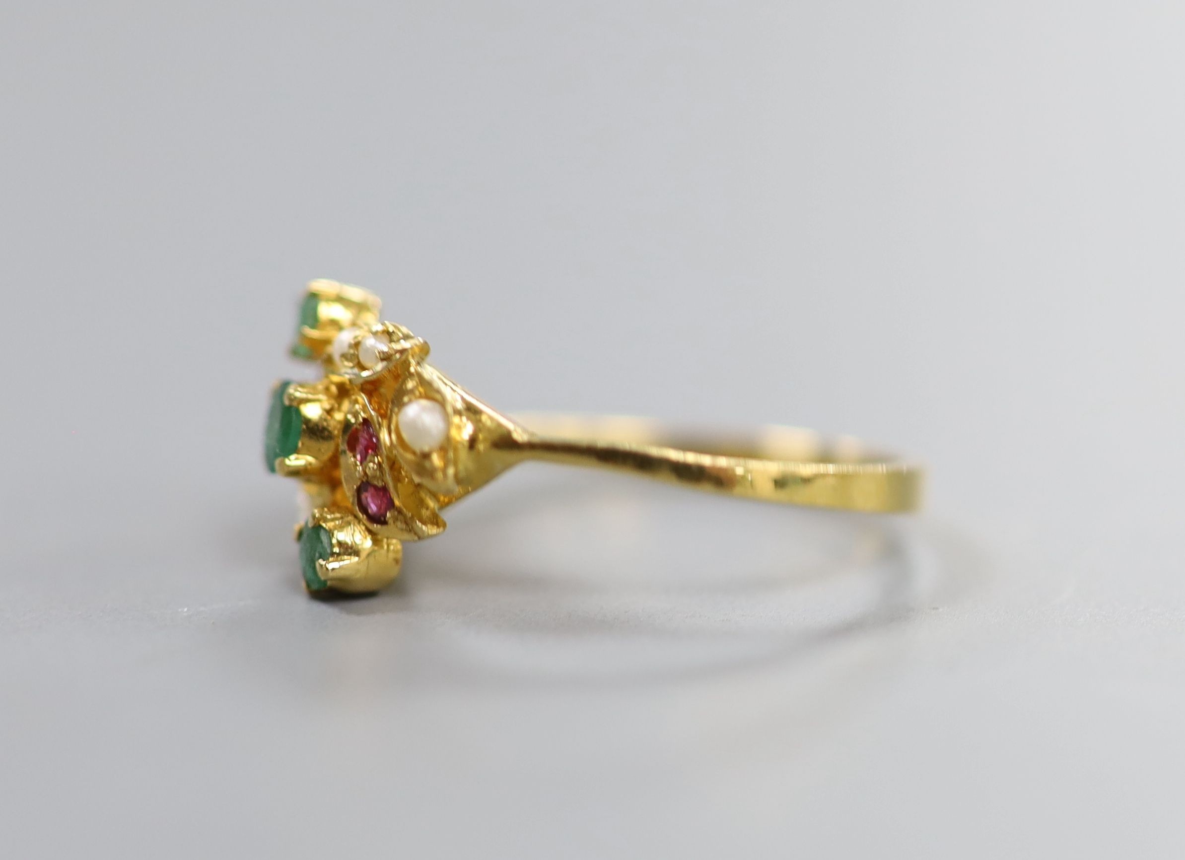 A modern yellow metal, emerald, ruby and seed pearl cluster set crossover ring, size L, gross weight 2.9 grams.